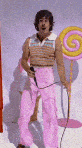 a man in pink pants is singing into a microphone in front of a lollipop
