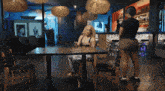 a woman sits at a table in a restaurant while a woman stands behind her