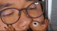 a man wearing glasses is kissing a small toy hamster on the nose .