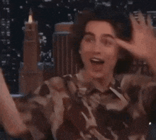 a young man in a camouflage shirt is making a funny face while holding his hands up in the air .
