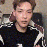 a young man is sitting in a chair and looking at the camera while wearing a black sweater .