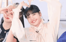 two girls are making a heart shape with their hands and smiling .