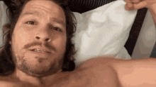 a shirtless man with long hair and a beard is laying in bed .