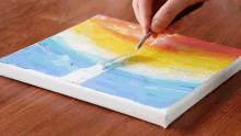 a person is painting a rainbow with a brush on a canvas
