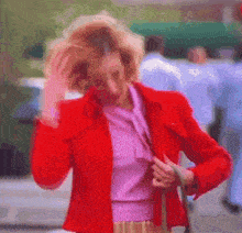 a woman in a red jacket and pink shirt is holding her hair