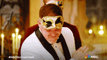 a man wearing a mask and a tuxedo with the nbc destination x logo