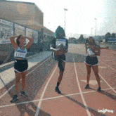 three athletes on a track with one wearing a number 0002