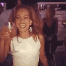 a woman in a white tank top is holding a glass of wine .