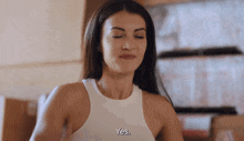 a woman in a white tank top says " yes " with her eyes closed