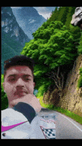 a man wearing a nike shirt stands in front of a mountain and road