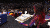 a woman with red hair is holding a cake in front of a crowd with the word live in the background