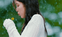 a woman in a white sweater is blowing a yellow flower in the rain .