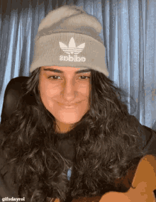 a woman wearing an adidas beanie is smiling and looking at the camera