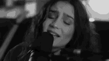 a black and white photo of a woman singing into a microphone with her eyes closed .