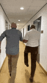 two men walking down a hallway with a fire alarm on the wall