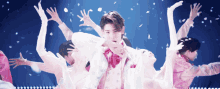 a man in a pink and white suit is surrounded by a group of dancers