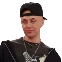 a man wearing a black hat and a necklace looks at the camera