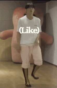 a man in a white shirt and pink shorts is standing in front of a giant stuffed animal with the word like on it