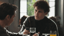 two men sitting at a table with a glass of orange juice