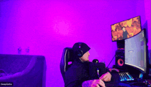 a man wearing headphones sits in front of a computer screen with a purple light behind him