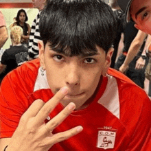 a young man in a red shirt is making a funny face with his finger to his mouth .