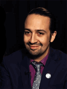 a man with a beard wearing a purple shirt and tie smiles for the camera