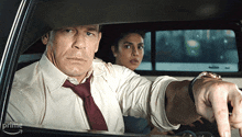 a man and a woman are in a car and the man is pointing
