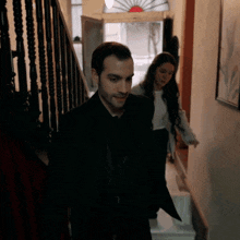 a man in a black suit is walking down stairs with a woman behind him