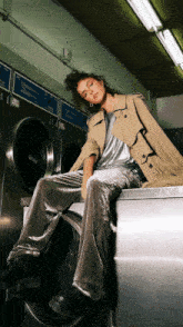 a woman in a trench coat sits on a washing machine in a laundromat with a sign that says dry