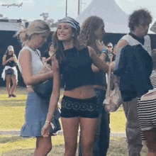 a woman in a crop top and shorts is standing next to another woman in a crowd of people .
