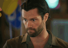 a man with a beard wearing a brown shirt looks at the camera