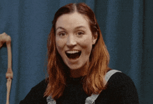 a woman with red hair is smiling in front of a blue wall