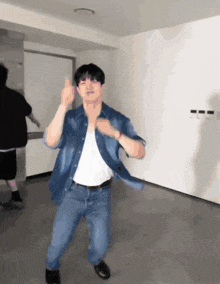 a man in a denim shirt and white shirt is dancing in an empty room