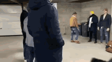 a group of people standing in a room with a man wearing a yellow hat