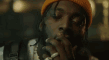 a man wearing an orange beanie is smoking a cigarette .