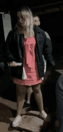 a woman in a pink dress is dancing with a man in a black jacket behind her .