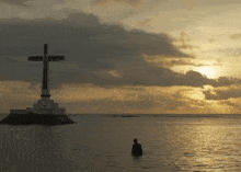 a cross in the middle of a body of water with a sunset in the background