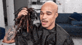 a bald man in a black cape is holding a bunch of dreadlocks .