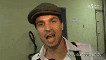 a man wearing a hat and suspenders is being interviewed on eurovision tv