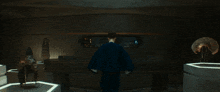 a woman in a blue shirt is standing in a dark room looking at the camera