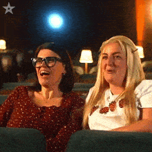 two women are laughing while watching a movie in a theater with a star in the corner