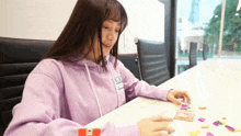 a woman in a purple hoodie is sitting at a table playing a card game .