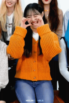 a girl wearing an orange sweater is making a face with her hands