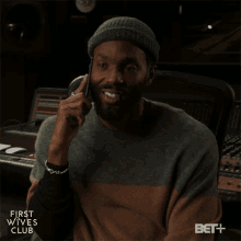 a man is smiling while talking on a cell phone with the first wives club logo in the corner