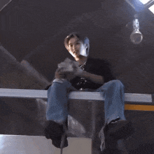 a man in a black shirt with the letter r on it is sitting on a railing with his arms up