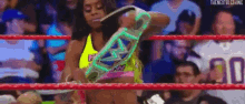 a woman is standing in a wrestling ring holding a glow in the dark championship belt .