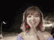 a woman wearing red earrings and a purple off the shoulder top is smiling
