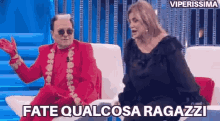 a man in a red suit is sitting next to a woman on a couch and talking to her .