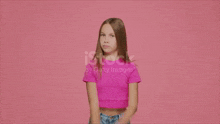 a girl in a pink crop top is flexing her muscles on a pink background .