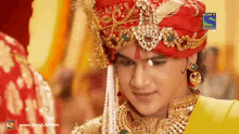 a man is wearing a red turban and gold jewelry with a sony television logo behind him